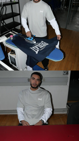 To billeder viser en mand iført en lysegrå Everlast t-shirt over en hvid langærmet trøje. Øverst står han ved et strygebord og stryger en mørk t-shirt med stort hvidt Everlast-logo. Nederst sidder han ved et bord med neutral mine, i samme outfit, foran en radiator.